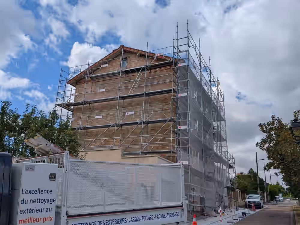 Immeuble en brique sous échafaudage, emprise de chantier balisée au sol