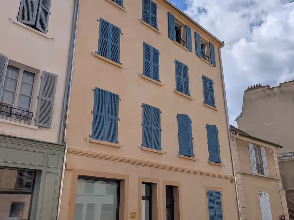 Immeuble de trois étages après intervention, enduit ocre et encadrements nets